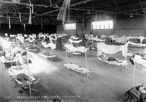 White patients sleeping on cots in airplane hanger