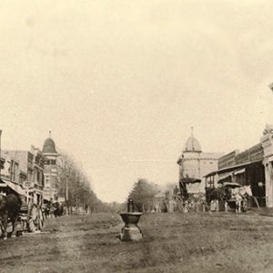 Dirt street with brick storefronts and horse drawn carriage