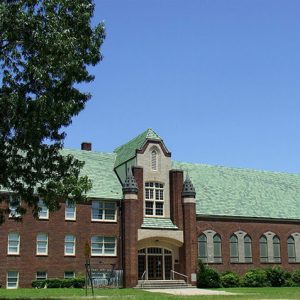 Multistory building with green sloped roof and arched doorway and arched windows