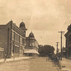 Men and horse drawn carriage on town street with multistory buildings on both sides