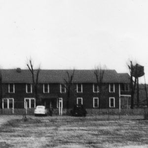 Long two-story building with trees and cars parked in front