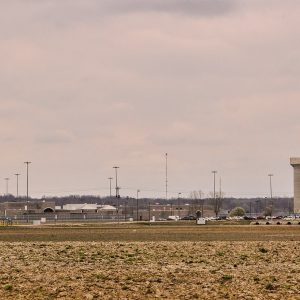 Distant view of single and multistory buildings inside fences with parking lot and water tower