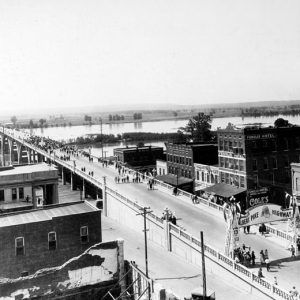 Crowd of people crossing a concrete bridge with buildings in the foreground with sign "Albert Pike Highway"