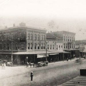 men and horse drawn carriages outside multistory buildings on town streets