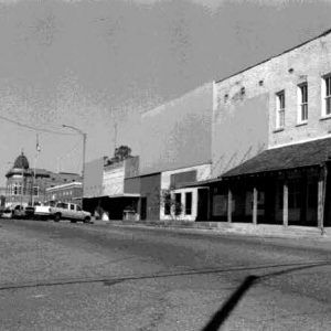 Multistory storefronts on street with parked trucks and multistory building with dome in the background