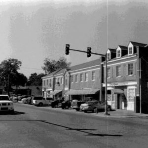 Traffic passing by multistory brick buildings with row of parked cars on street with traffic lights