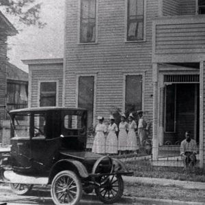 African-American men and nurses outside multistory wooden building with car parked on the street