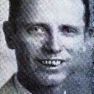 Smiling white man with brown hair and slightly crooked teeth in suit jacket and tie