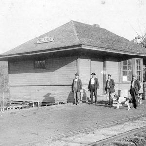 Four white men and dog at train depot building with tracks