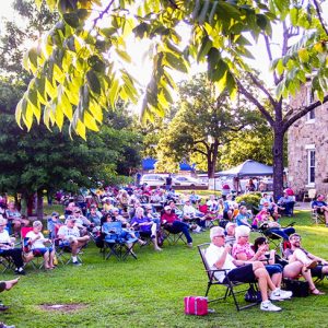 Crowd of men and women spectators in lawn chairs sitting outside multistory building