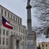 Stone monument with soldier holding gun atop a pedestal next to flag