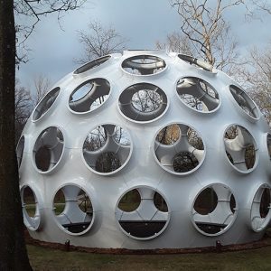 White geodesic dome with round holes and bare trees in the background