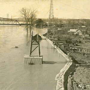 River almost overflowing levee with people standing among houses