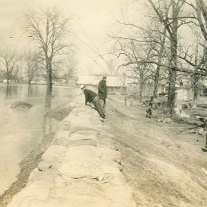 Two men examining levee next to overflowing river