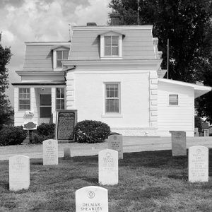 Two-story building with plaque and gravestones in front