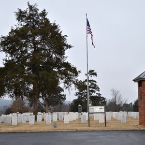 Trees flag pole and brick tower with plaque in cemetery