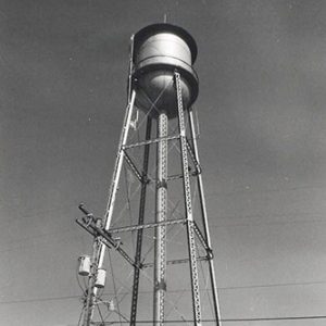 Looking up at water tower with power lines and outbuildings below it