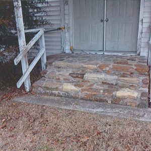 Stone steps under covered entrance with wooden railings and double doors