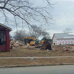 Single-story house next to demolished house and construction equipment on street