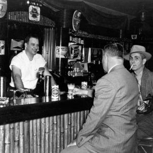 White bartender serving two white men in suits at hotel bar