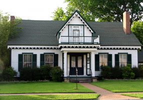 Wood frame two story house ornate triangle pattern roof line  balcony and chimneys on opposite ends with manicured lawn