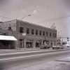 Cars driving by two-story building with storefront and windows on street corner