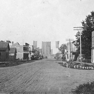 Multistory buildings and houses on dirt road with American flags hanging above it