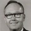 White man with glasses smiling in suit and tie