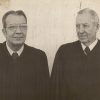 Older white man with glasses standing next to older white man with both wearing judge's robes