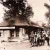 Group of men with cart outside single-story railroad building