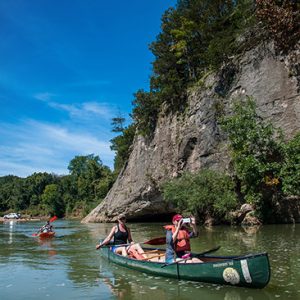 Canoeists on river next to rock wall