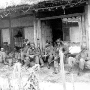 Mixed group of men in military uniforms resting outside Korean house