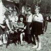 White woman posing with young white girls in matching uniforms with goat outside house