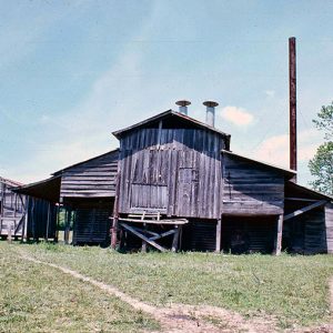 Weathered barn-like building with smokestacks in field