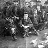 Group of white men in suits and hats sitting in front of pigeons