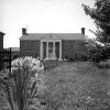 Two-story house with covered porch supported by four columns with flowers and gate in the foreground