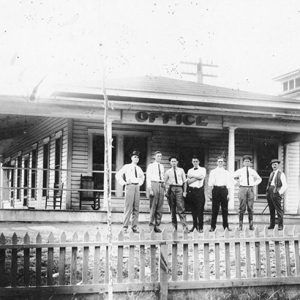 Group of white men in front of office building with fence