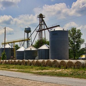 Row of hay bales in front of grain elevator and silos with water tower in the background