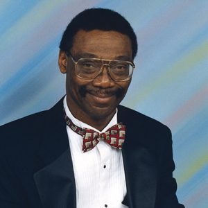 African-American man with glasses and mustache smiling in suit and bow tie