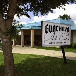 Long single-story building with tree and sign under a tree