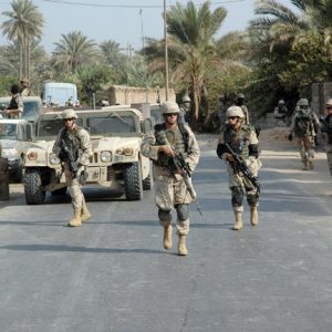 Male soldiers patrol city street with military vehicle and palm trees in background