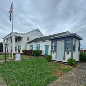 Multistory building with covered entrance and white siding next to blue and white guard house