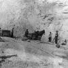 Group of men with horses, track-based carts, in open-pit mine