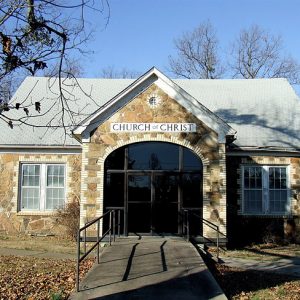 Single-story stone building with arched entrance and "Church of Christ" written above the glass doors