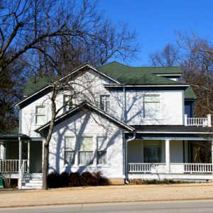 white house with green gabled roof and wrap around porch