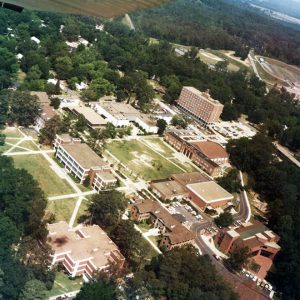 Aerial view of brick buildings on a campus with quads roads baseball field and forests