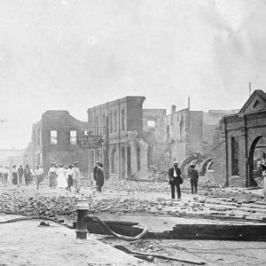 Crowd of people in street after a fire surrounded by debris and destroyed buildings