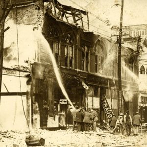 Firemen using water hoses to put out fire on row of burning buildings