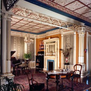 Ornate room with piano, decorative tile ceiling, columns, and wooden furniture on large rug and wood floors