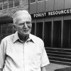 Older white man in glasses outside wood and brick building